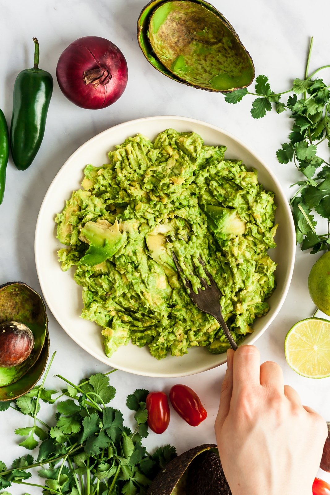 mashing avocado next to ingredients for the best guacamole