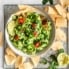 the best guacamole in a white bowl next to tortilla chips