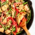 orange chicken stir fry in a skillet pan with a wooden spoon