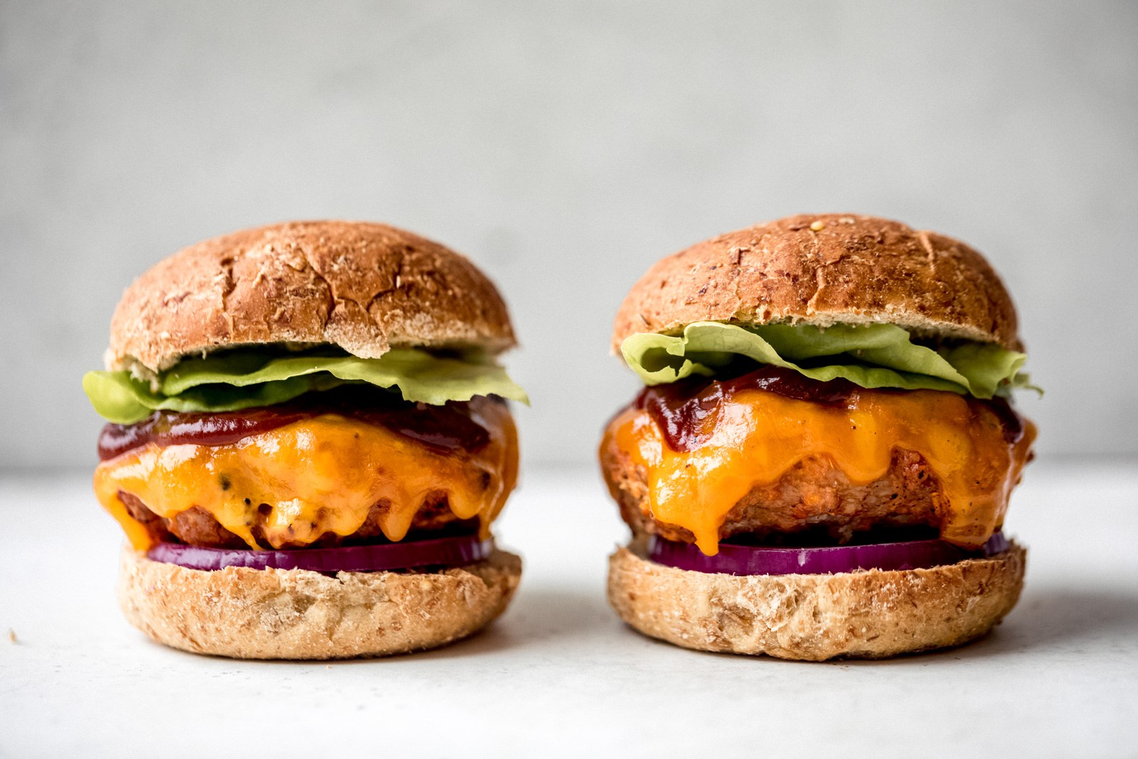 two bbq chicken burgers next to each other topped with cheese, bbq sauce, and lettuce
