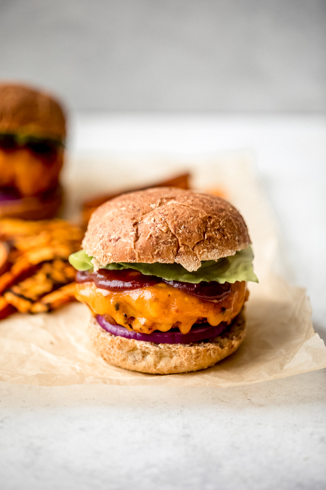 sweet potato chicken burger topped with cheese, bbq sauce, and lettuce on parchment paper with sweet potato fries