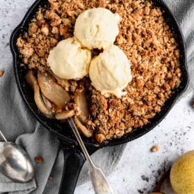 healthy pear crisp in a skillet topped with ice cream