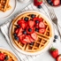 classic buttermilk waffle topped with berries on a plate next to a bowl of berries