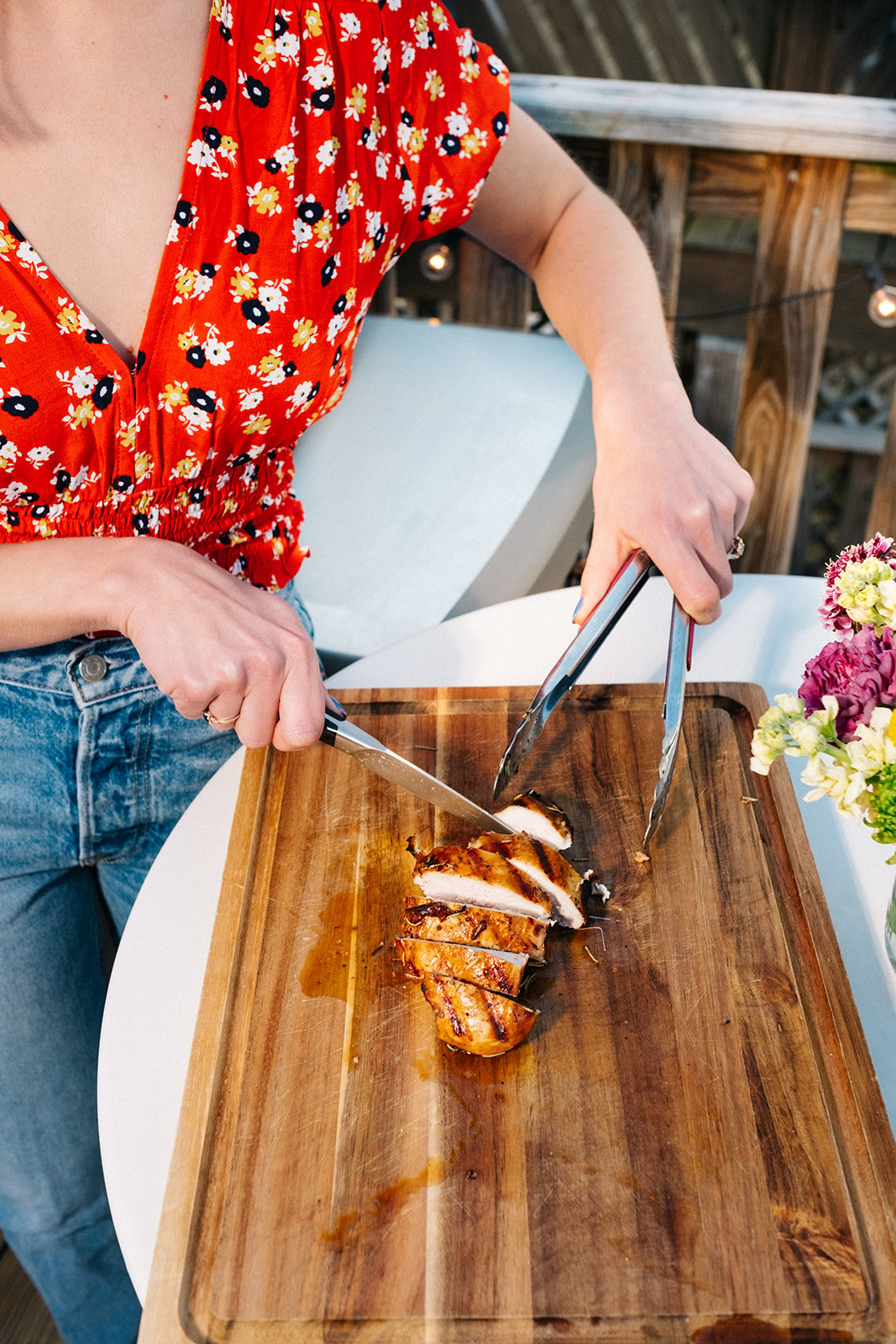 woman cutting a grilled chicken breast on a wooden cutting board