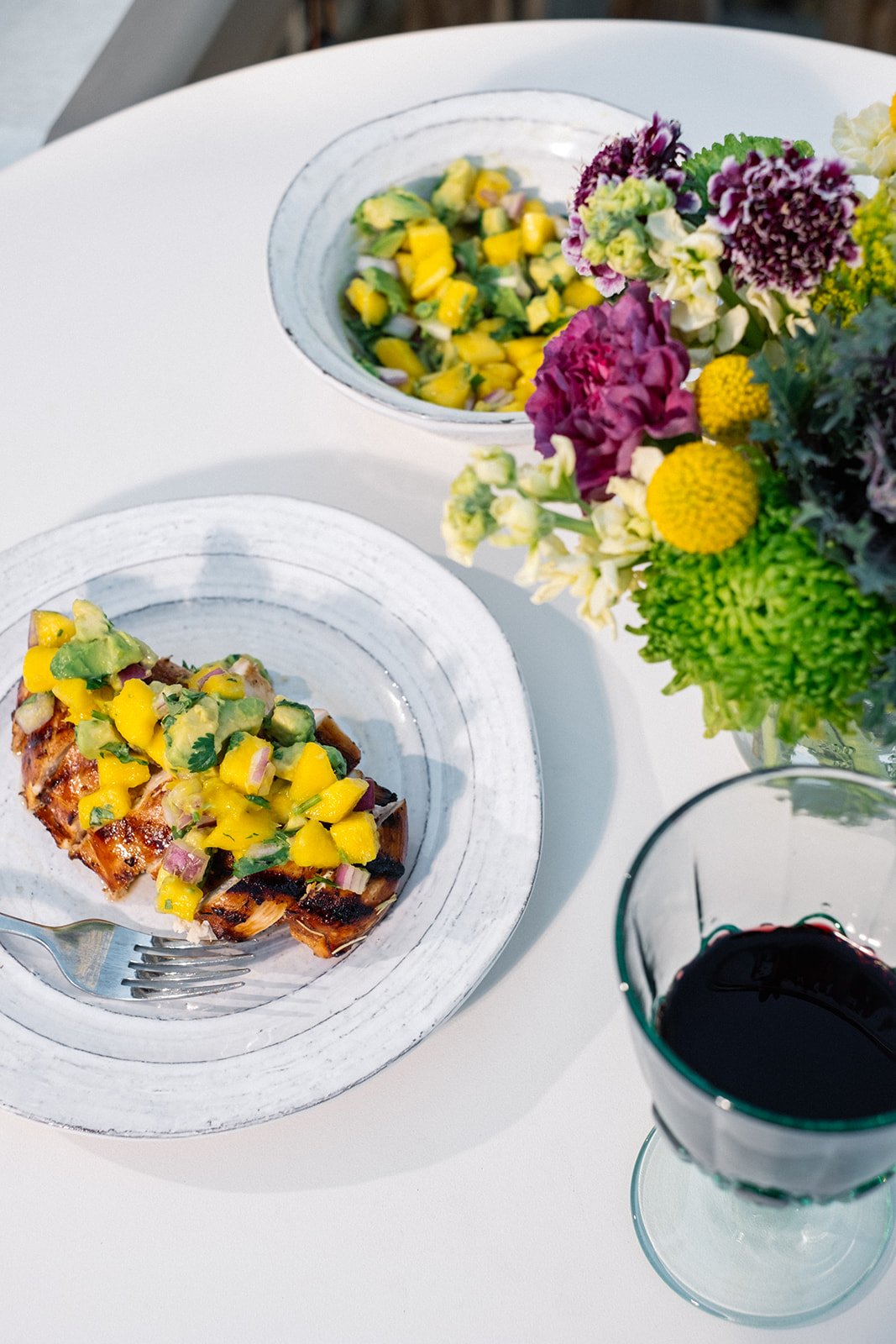 grilled chicken on a plate topped with pico next to a bunch of flowers