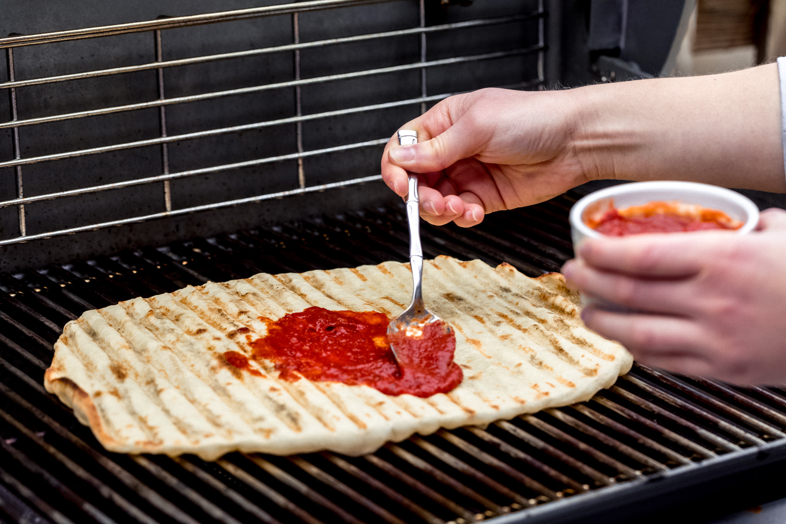 adding tomato sauce to a pizza on the grill 