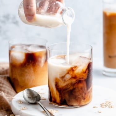 pouring homemade oat milk into a glass of iced coffee