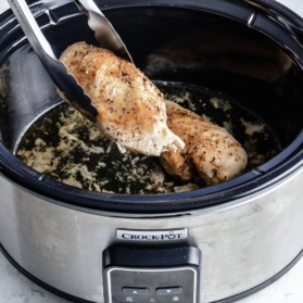 pulling a chicken breast out of a slow cooker