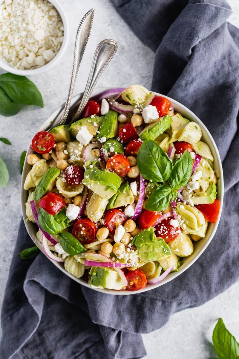 chickpea pasta salad in a bowl with avocado, tomatoes, red onion and feta