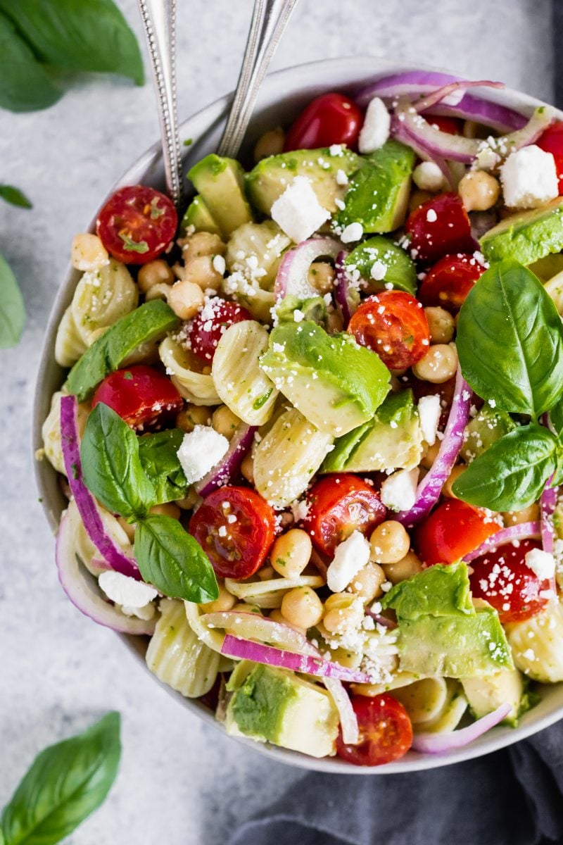 mediterranean chickpea pasta salad in a bowl with avocado, tomato, red onion and feta