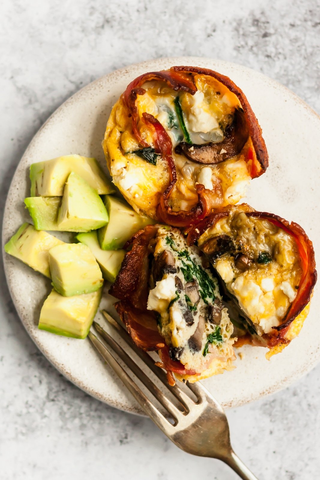 bacon egg muffin cups with avocado cubes on a plate with a fork