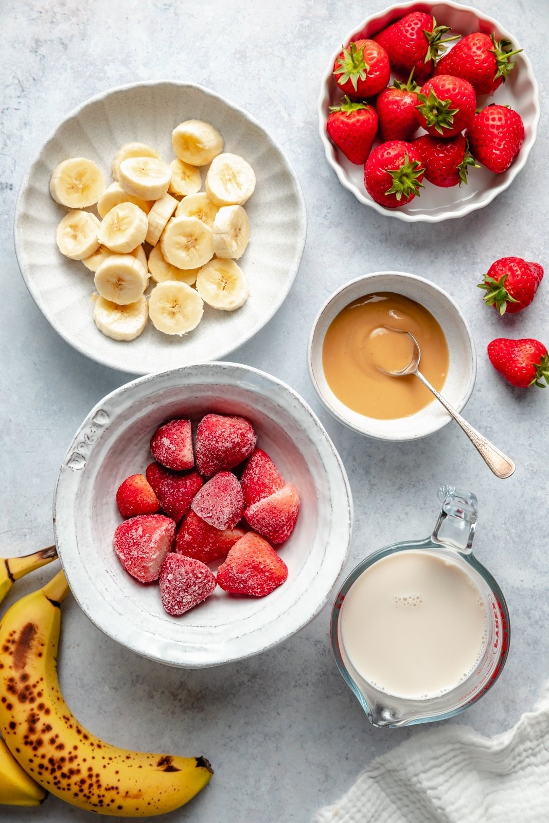 ingredients for a strawberry banana peanut butter smoothie in bowls