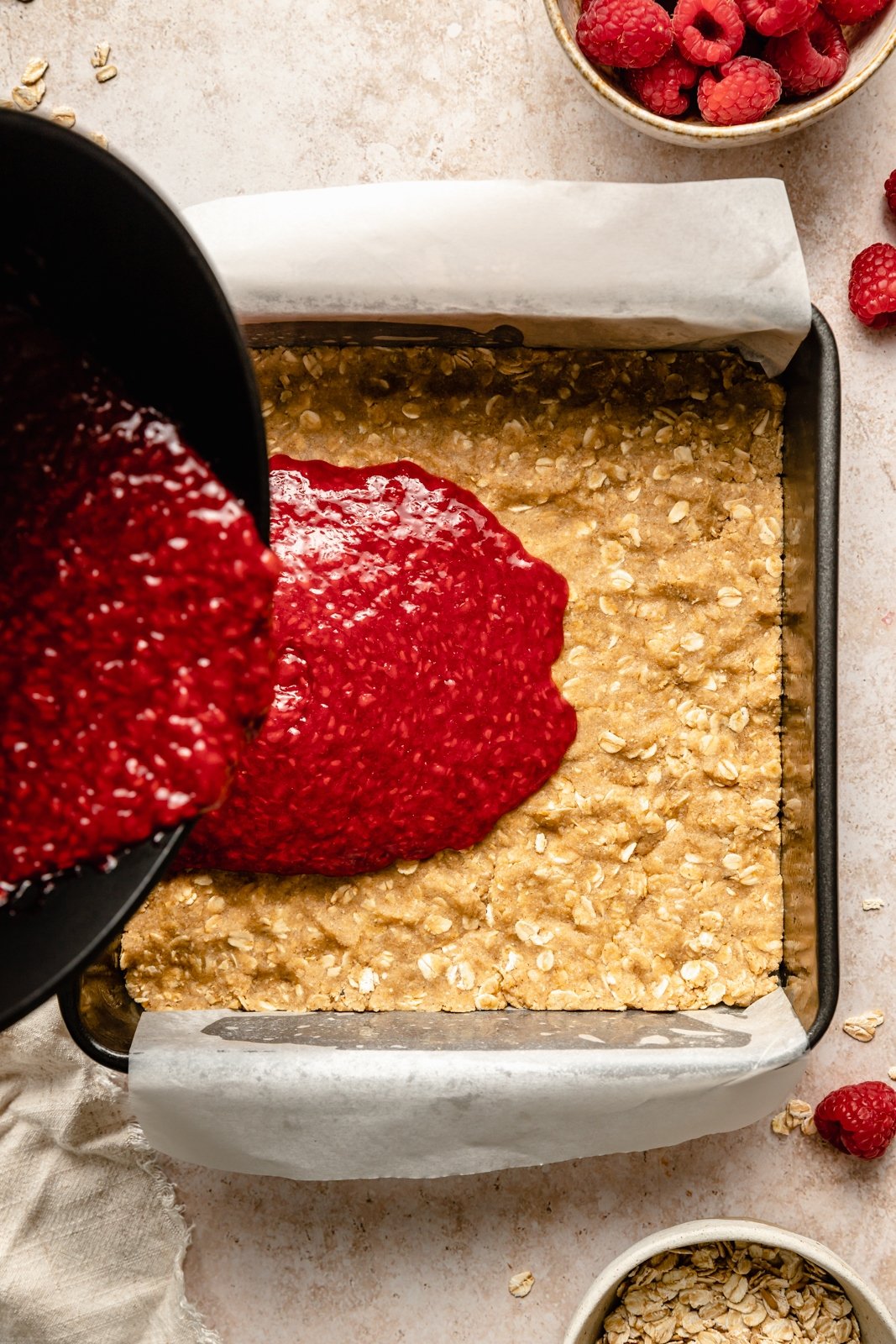 pouring raspberry filling into a crust for healthy raspberry pie bars