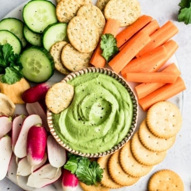 spicy green cashew dip on a platter with veggies and crackers