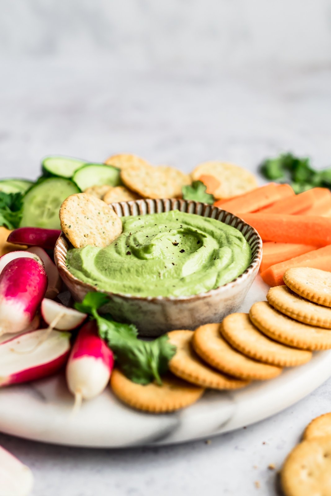 spicy green cashew dip on a platter with a cracker in it