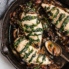 three spinach stuffed chicken breasts in a skillet with a spoon