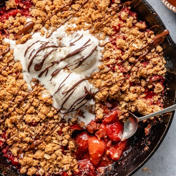strawberry crisp in a skillet topped with ice cream