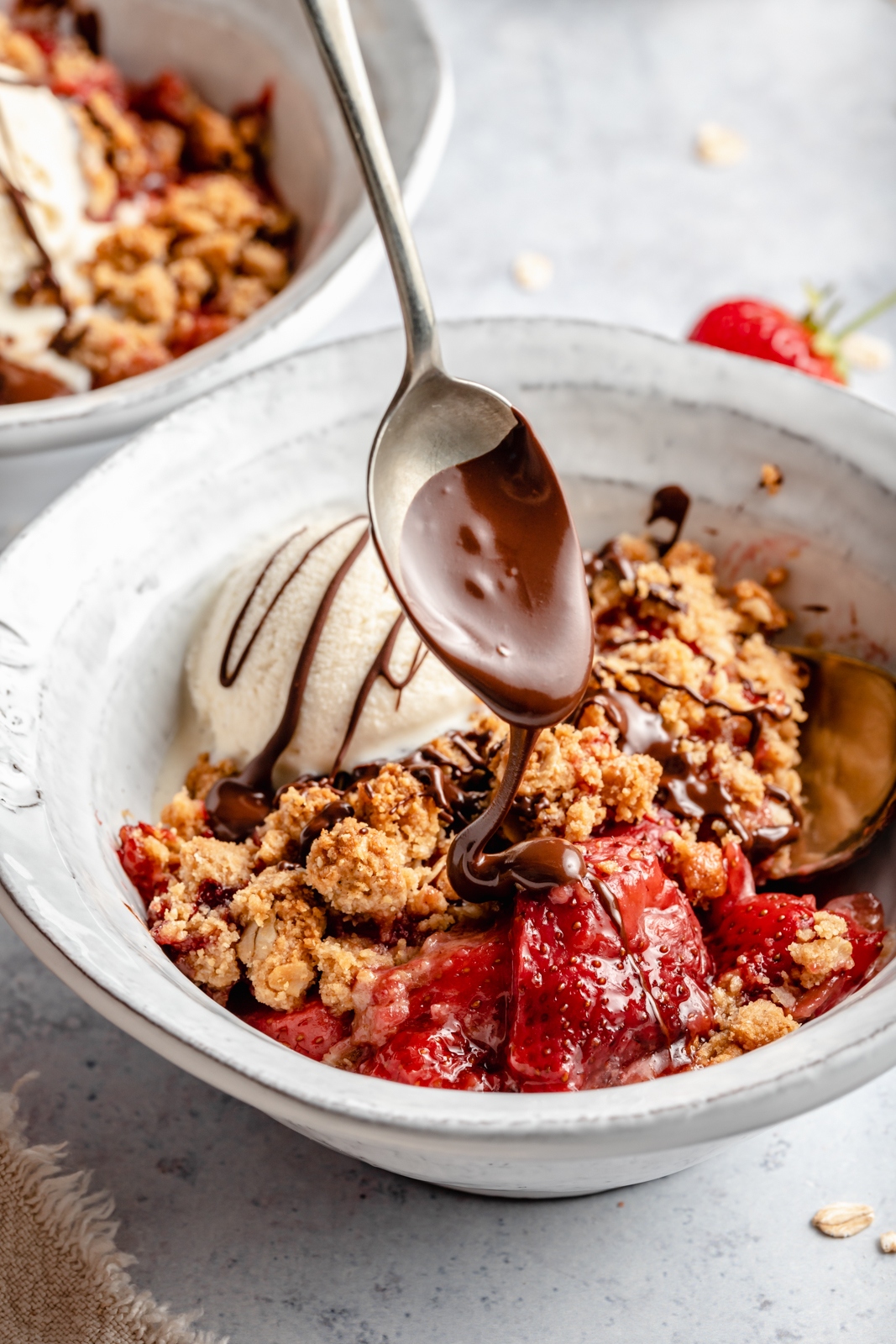 drizzling chocolate into a bowl of strawberry crisp