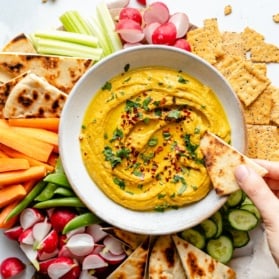 dipping pita into a bowl of homemade curry hummus
