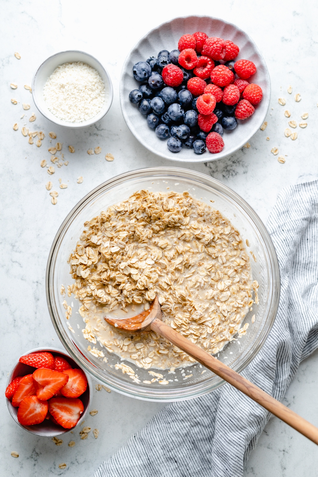 mixing oatmeal next to bowls of berries for berry baked oatmeal