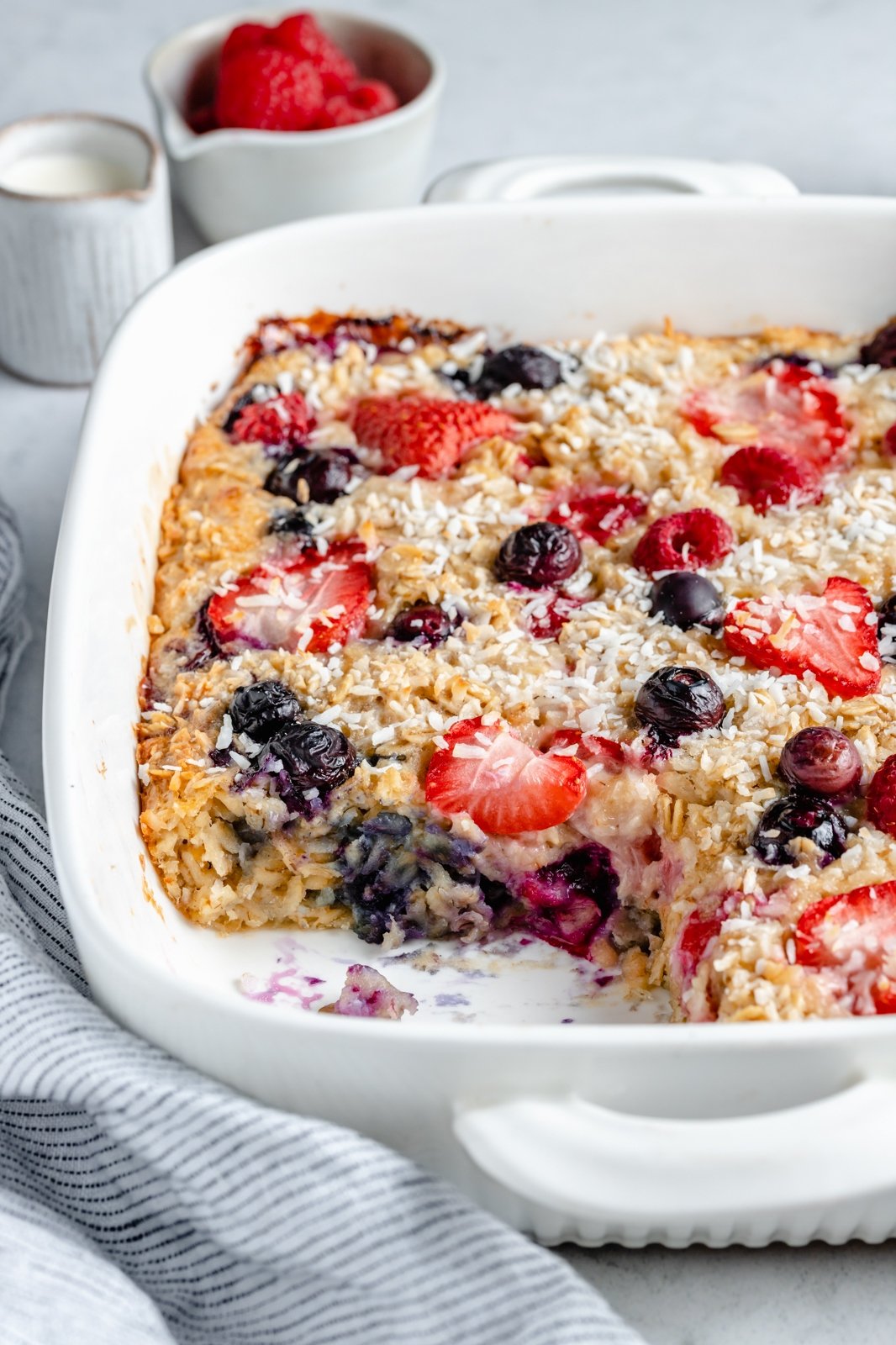 berries and cream baked oatmeal in a baking dish with a slice cut out