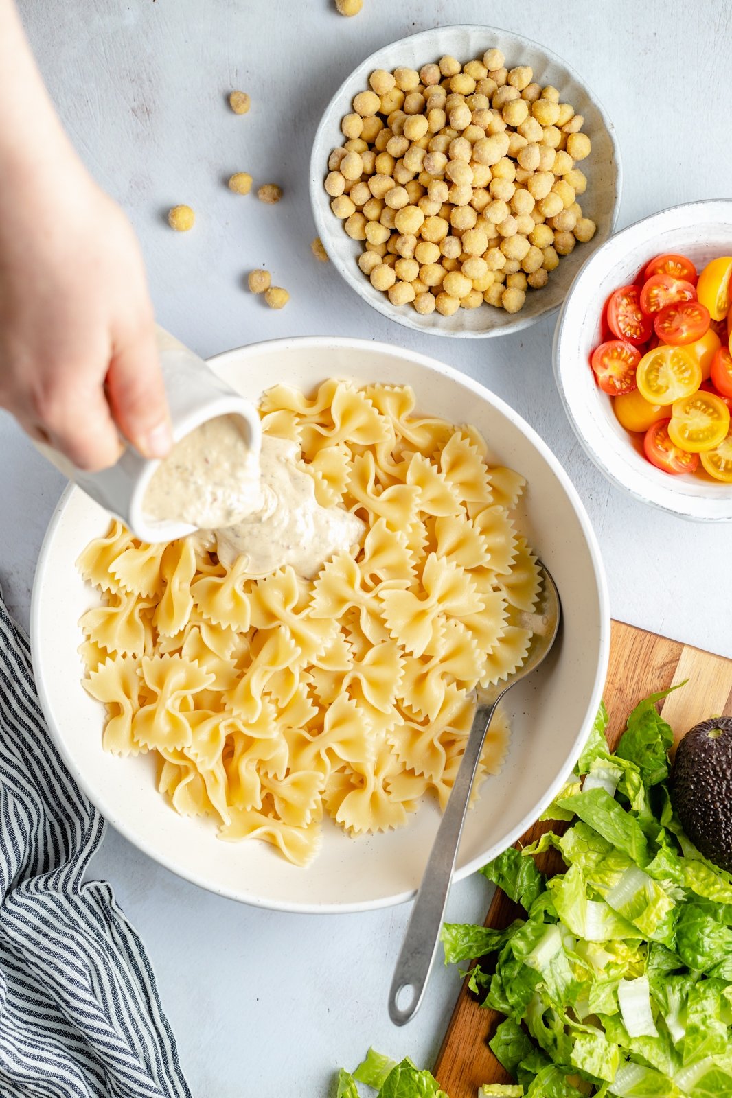 pouring dressing into a bowl of pasta for vegan caesar pasta salad