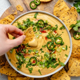 dipping a chip into a bowl of vegan butternut squash queso
