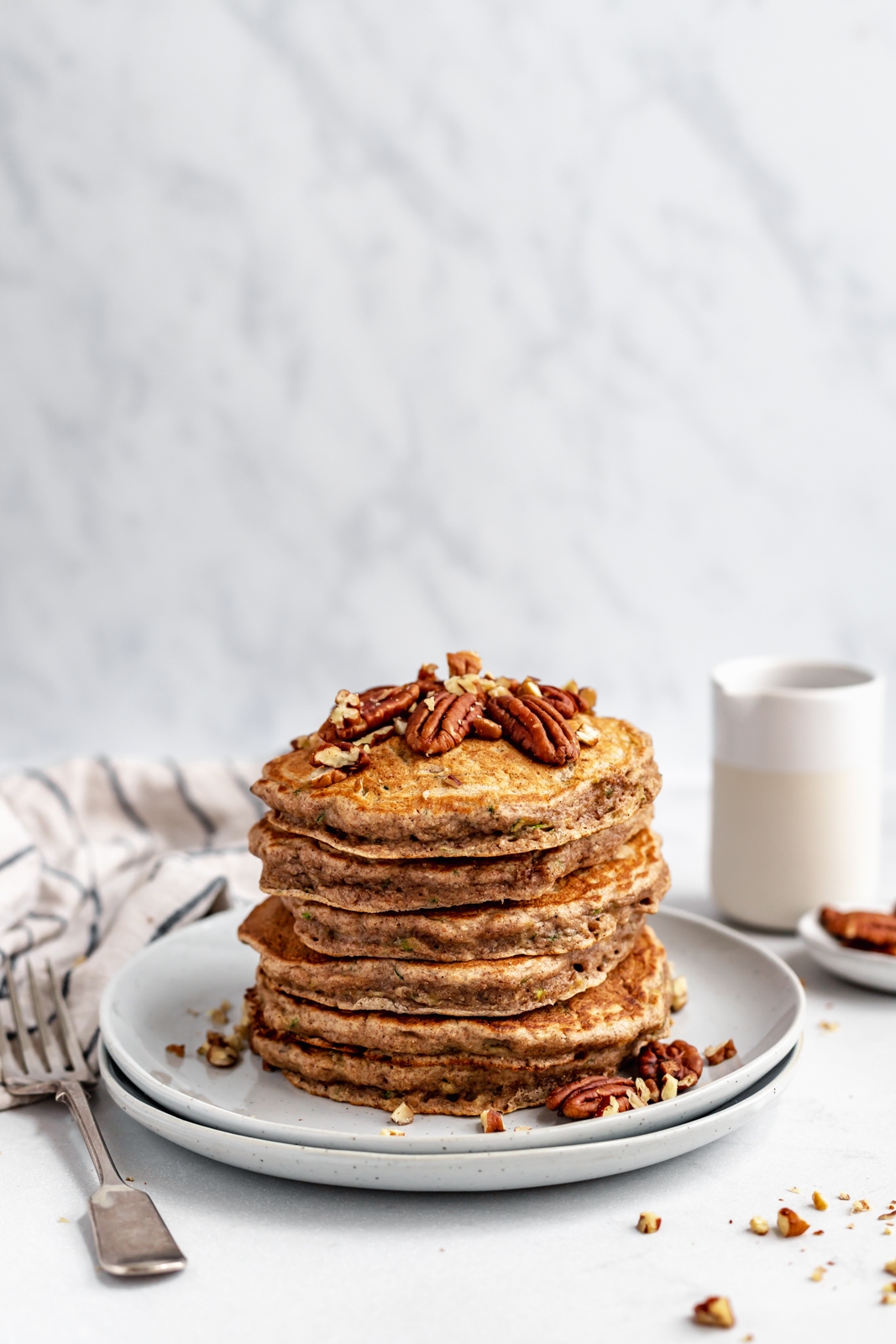 stack of healthy zucchini bread pancakes topped with pecans on a plate